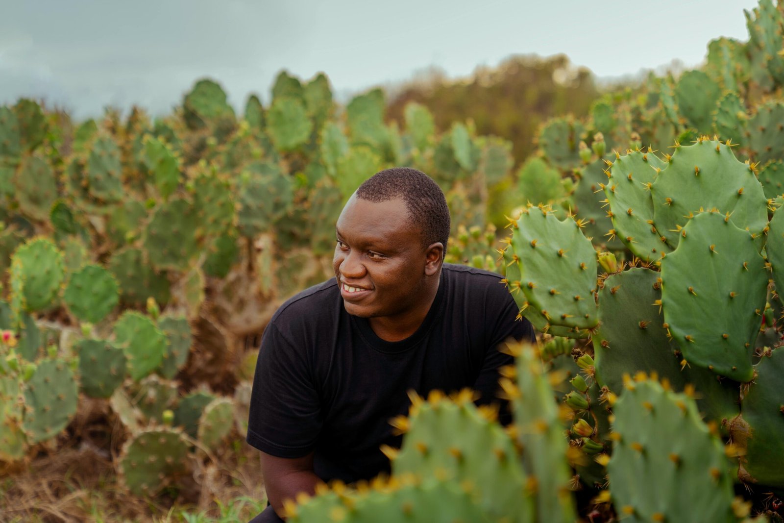 A cheerful man surrounded by cacti in lush greenery in Tanzania sunshine.